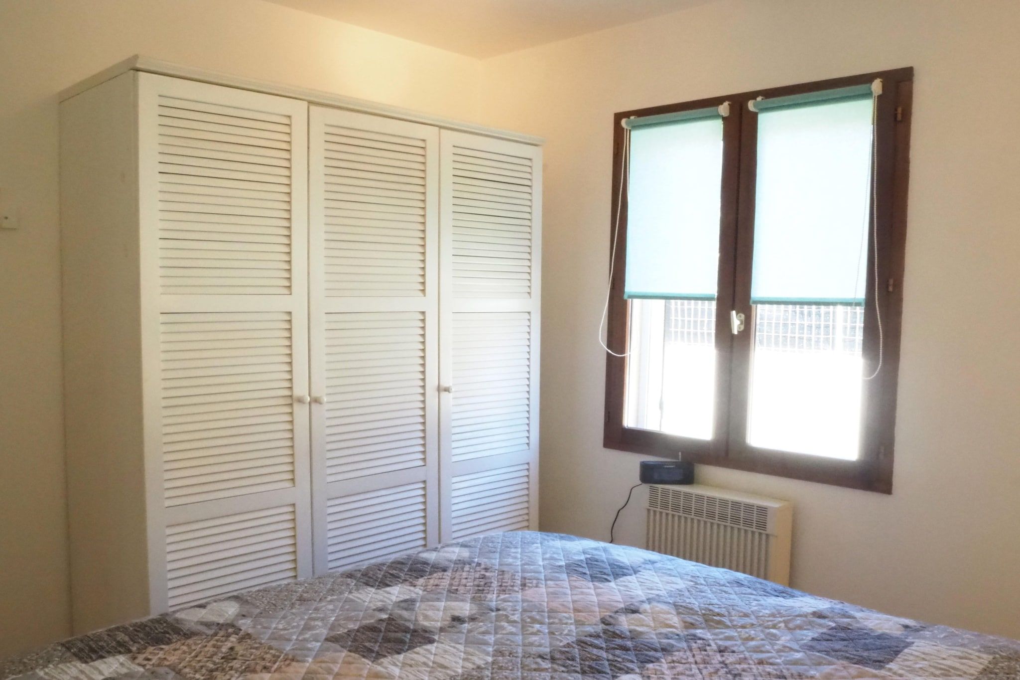 A bedroom with a bed, a wardrobe, and a window with blinds.