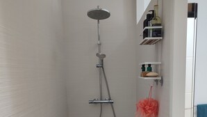 Un baño moderno con ducha, inodoro y lavamanos. Hay artículos de aseo en un estante y una toalla colgada en la pared.