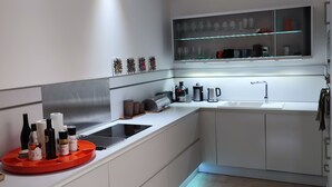 Una cocina moderna con armarios blancos, una campana extractora de acero inoxidable y una bodega para vinos empotrada sobre el lavamanos.