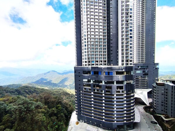 Um edifício alto com vários andares, cercado por vegetação exuberante e montanhas ao fundo.
