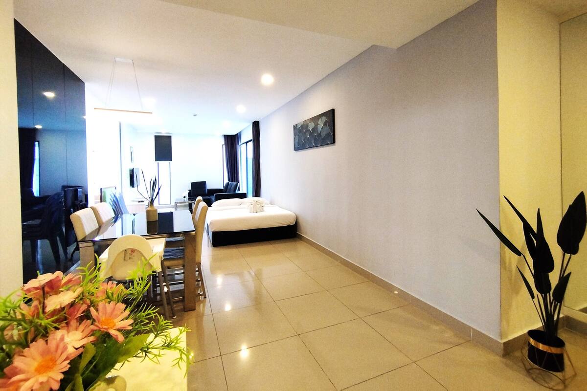 A modern hotel room with a bed, a dining table with chairs, a small desk, and a large window.