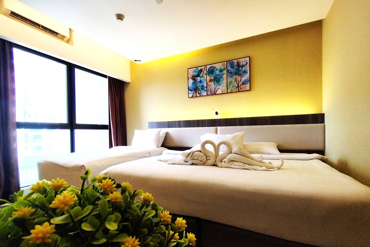 A hotel room with a large bed, a headboard, a window with curtains, a wall-mounted air conditioner, and a painting above the bed.
