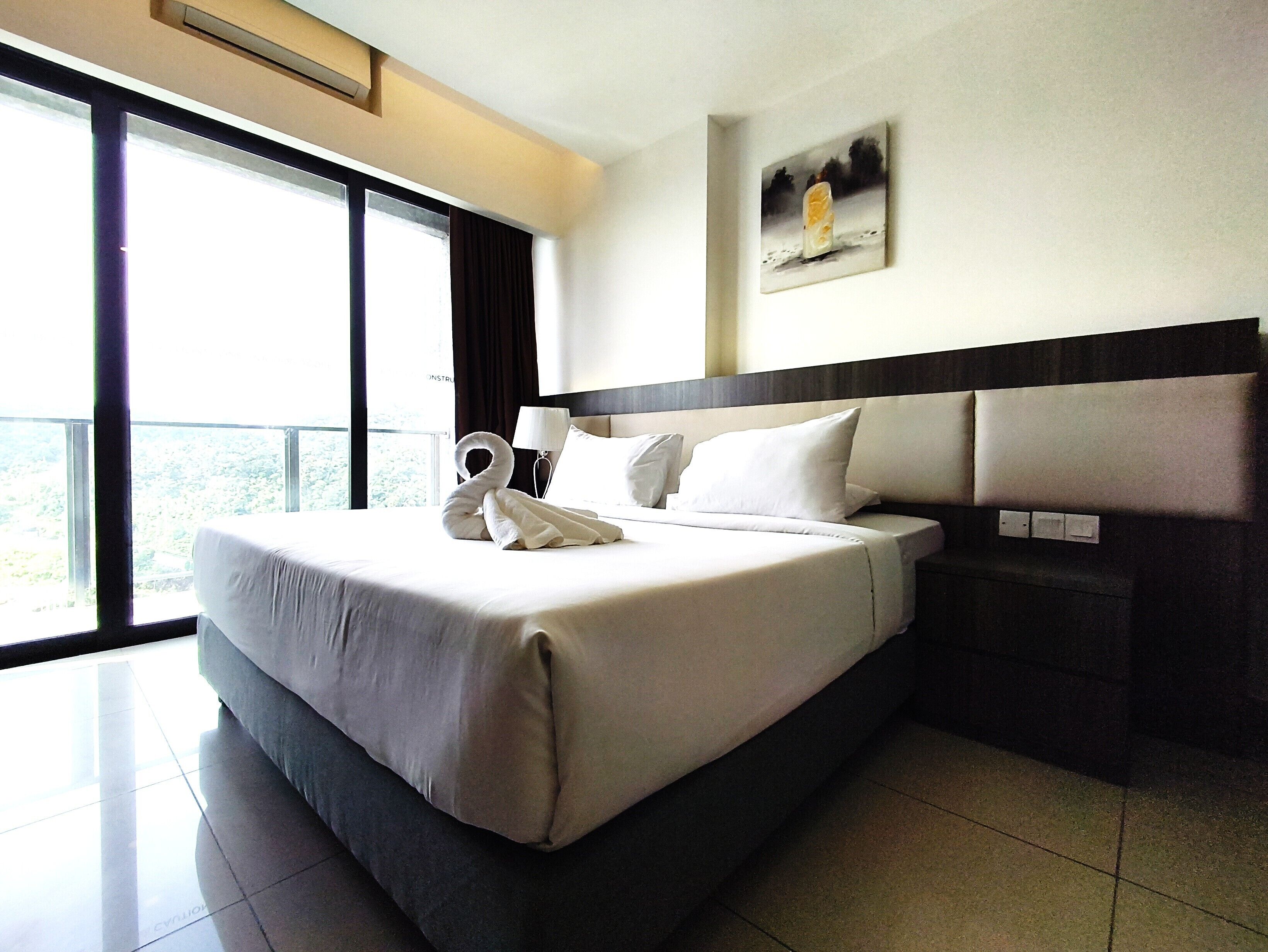 A hotel room with a large bed, a nightstand, a lamp, a painting, and a view through a large window.