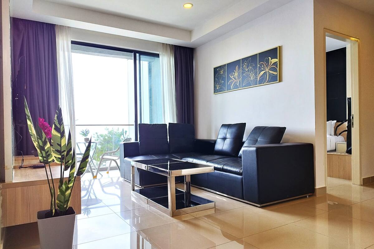 A modern living room with a black leather sofa, a coffee table, and a potted plant.