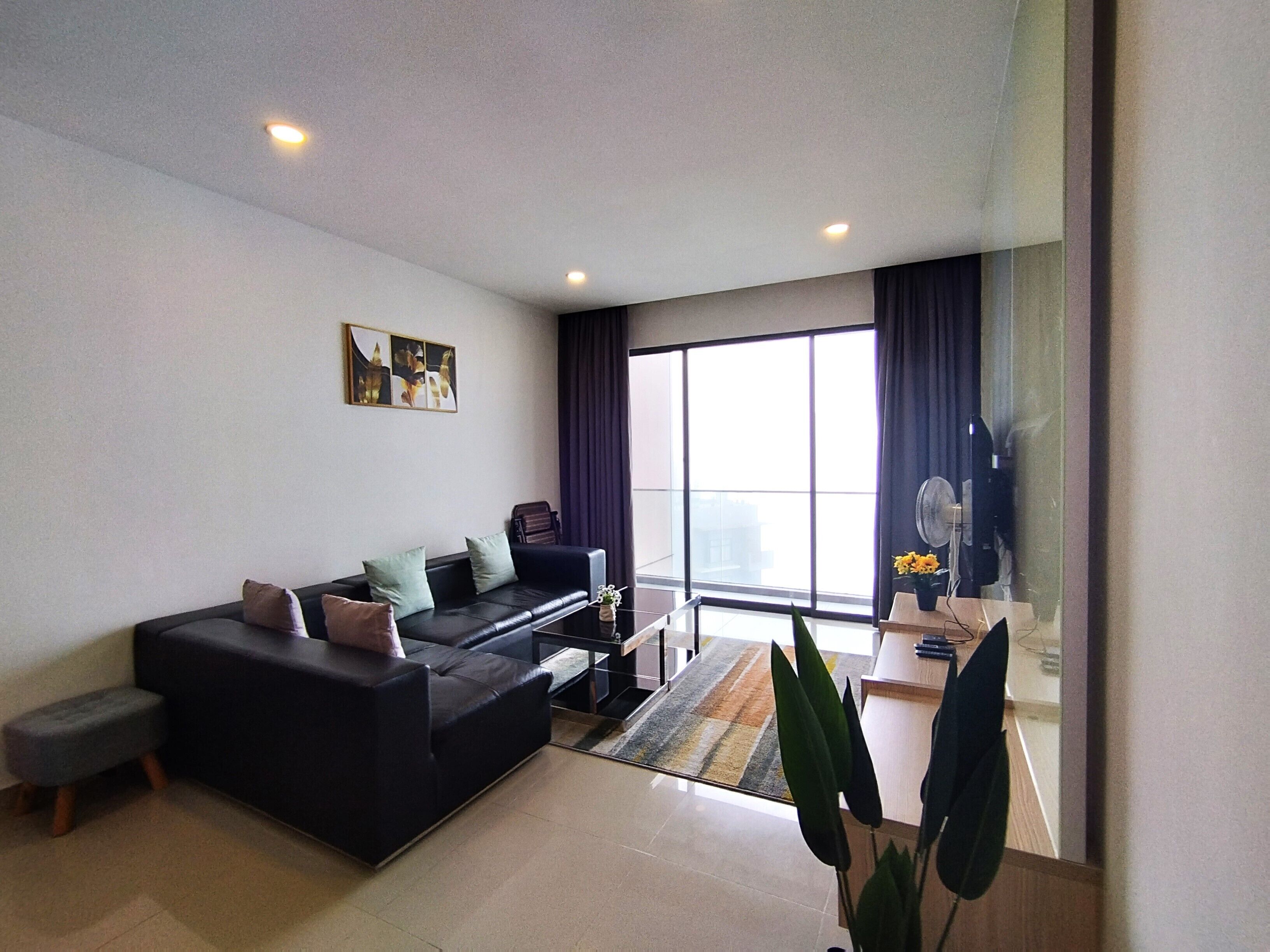 Una sala de estar moderna con un sofá negro, una mesita y un ventanal con cortinas.