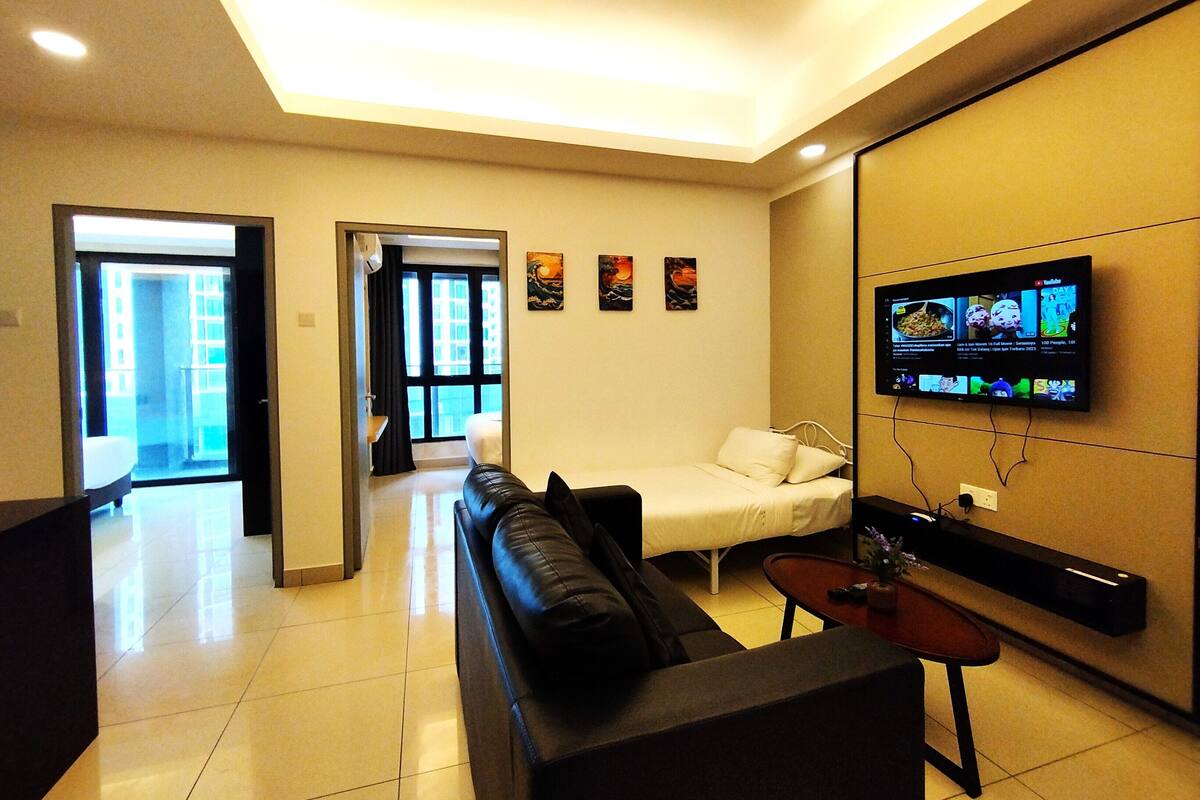 A hotel room with a sofa, a bed, a TV mounted on the wall, and a small table with a vase.
