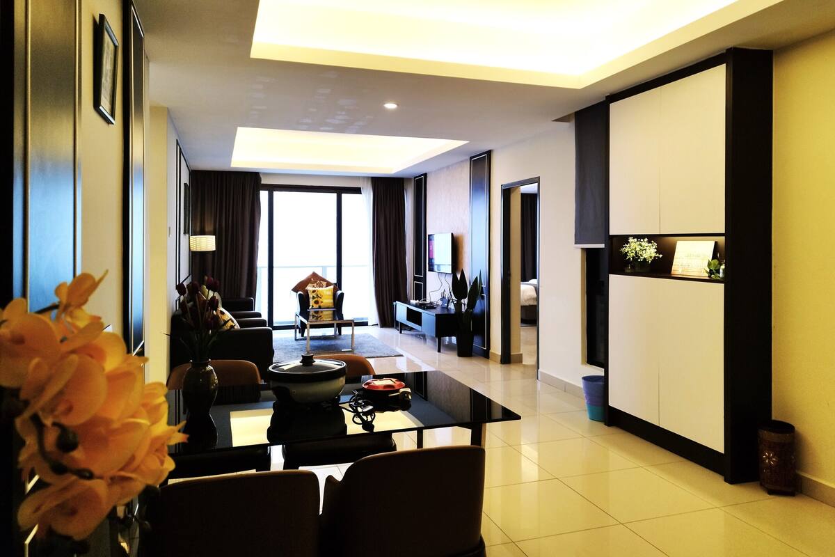 A modern hotel room with a dining area, a living room, and a large window providing a view.