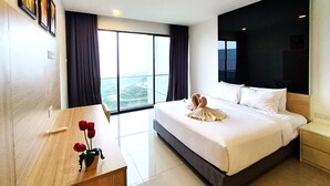 Ein Hotelzimmer mit einem großen Bett, einem Holztisch, einer Vase mit roten Blumen und Blick ins Freie durch große Fenster.