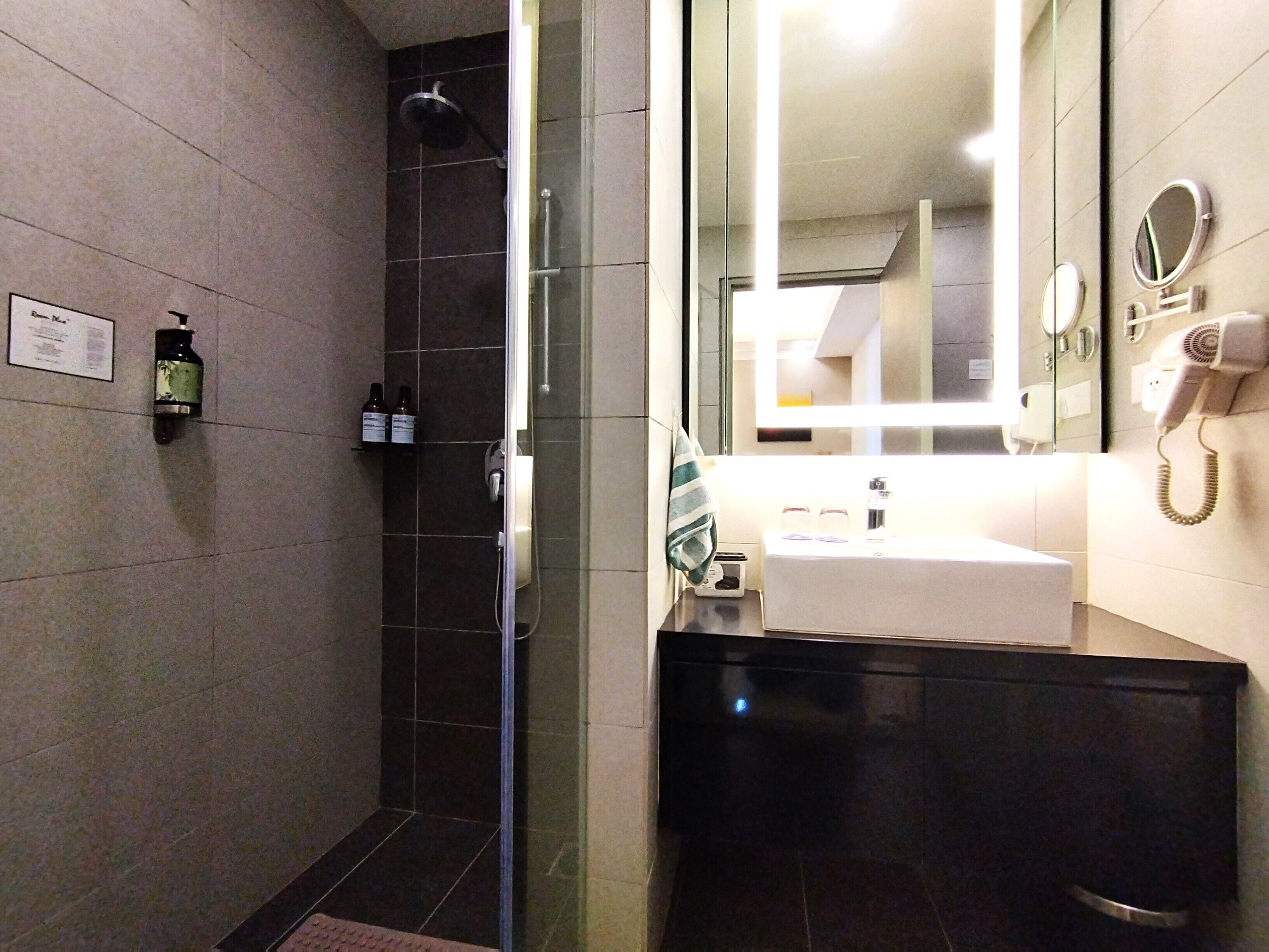 A modern bathroom with a glass shower enclosure, a sink with a mirror, and a hairdryer on the wall.