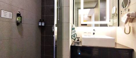 A modern bathroom with a glass shower enclosure, a sink with a mirror, and a hairdryer on the wall.
