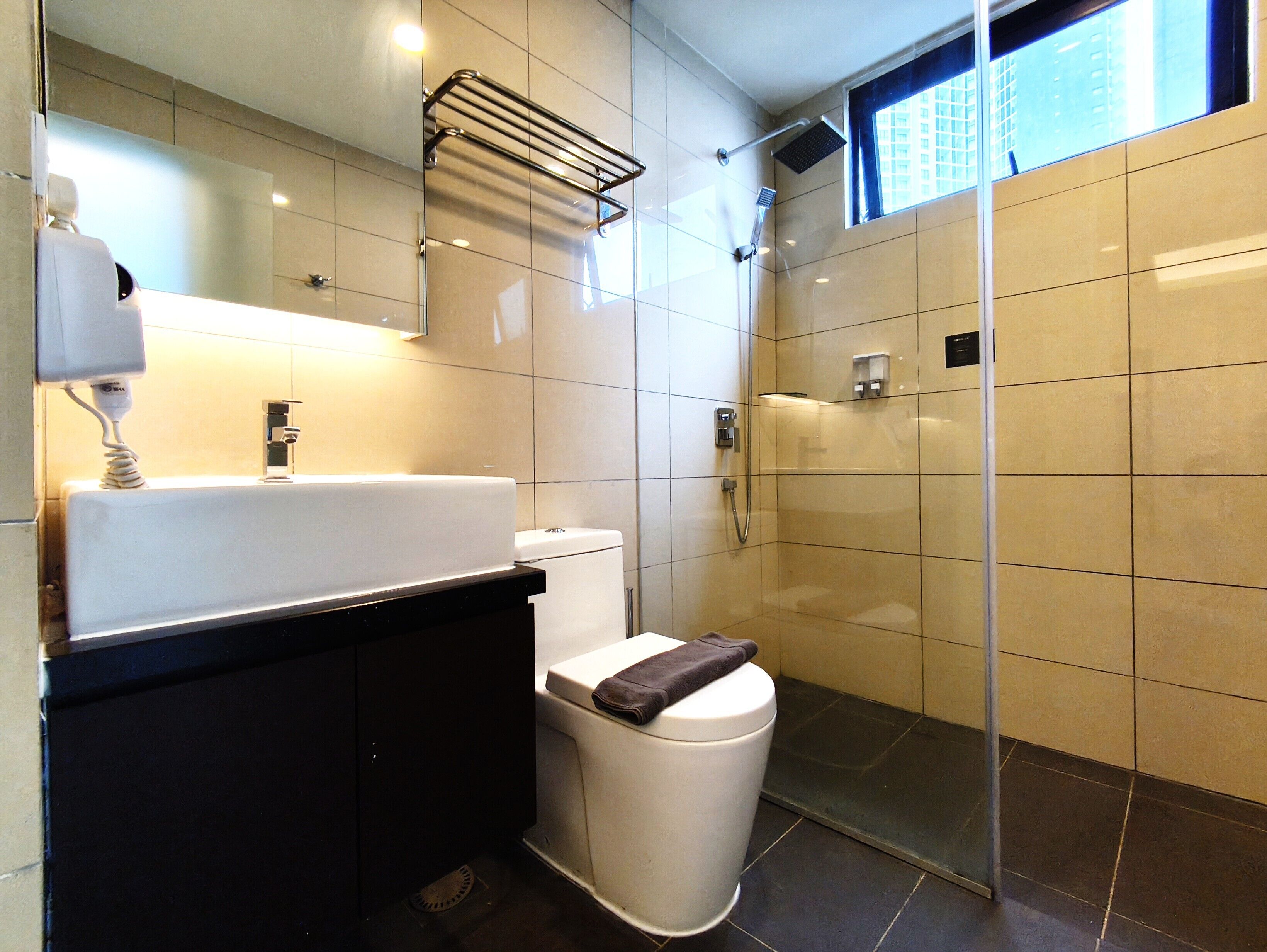 A modern bathroom with a white sink, black countertop, and a glass shower enclosure.