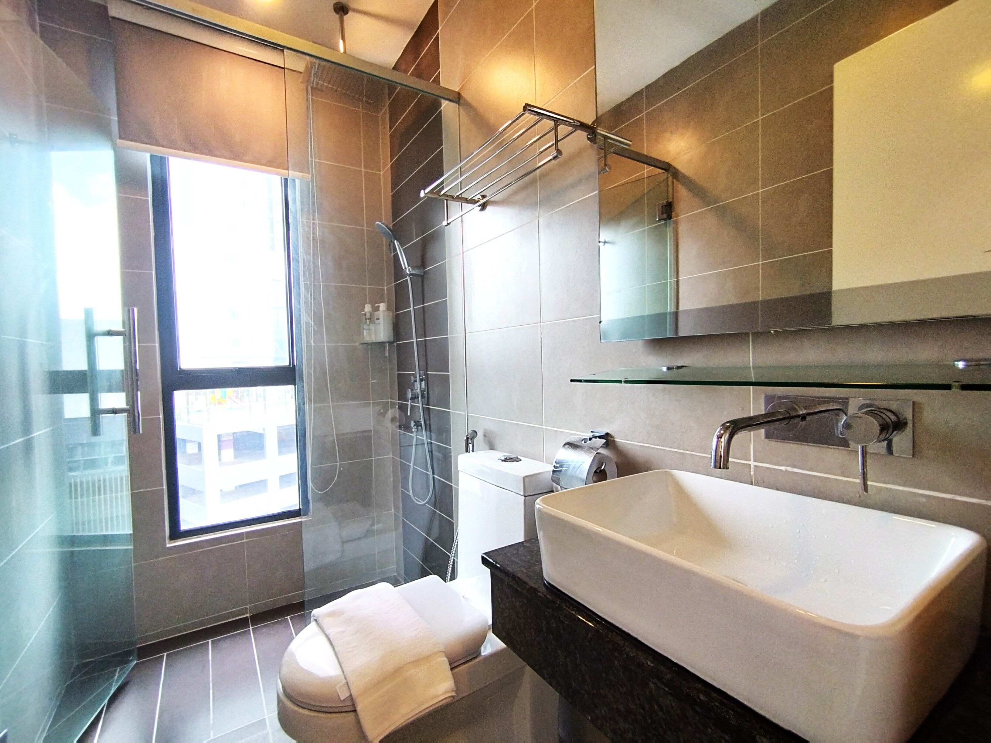 A modern bathroom with a glass shower enclosure, a large bathtub, a toilet, and a glass shelf above the sink.