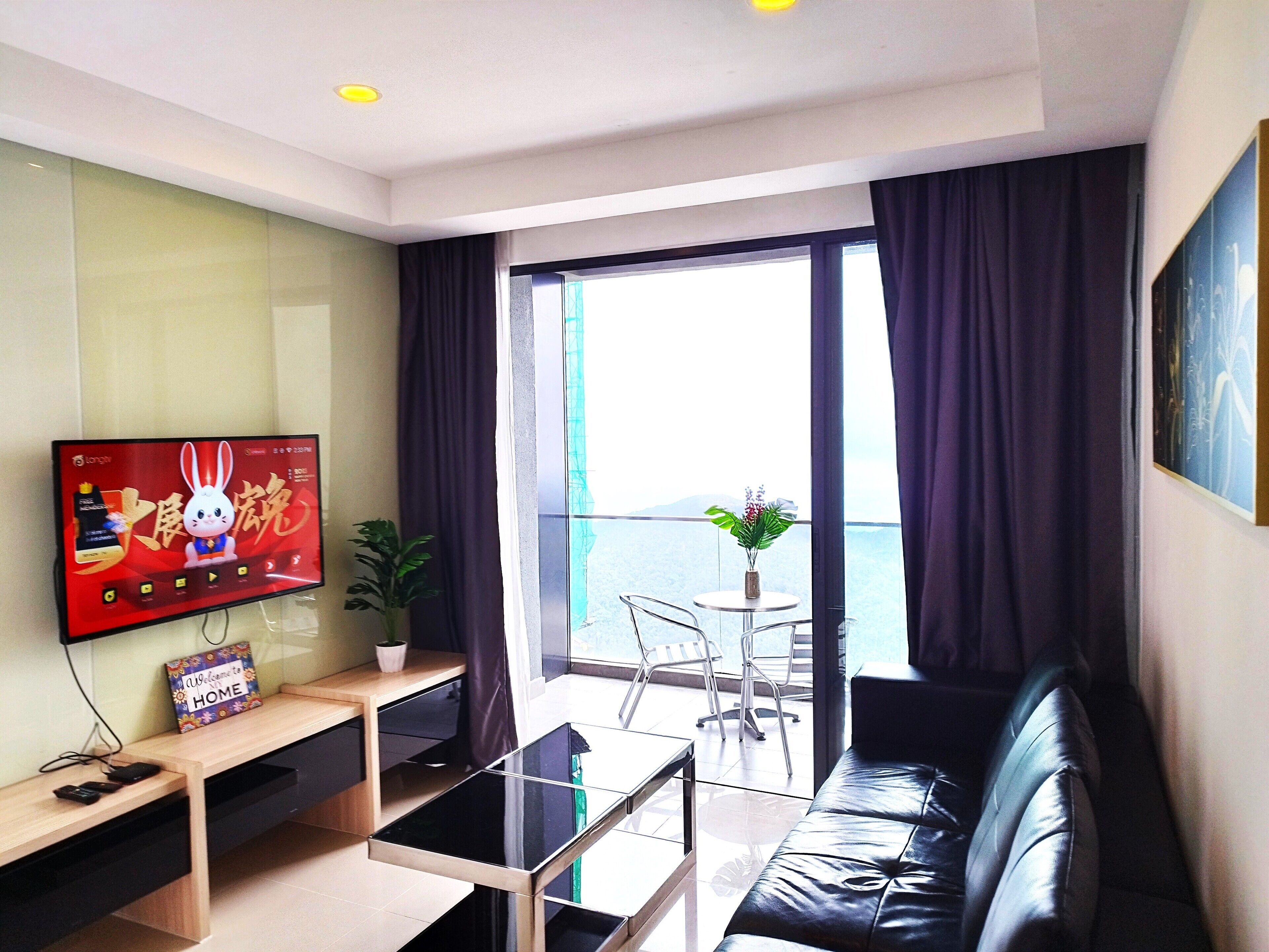 A modern living room with a flat-screen TV, a sofa, a coffee table, and a balcony with a view.
