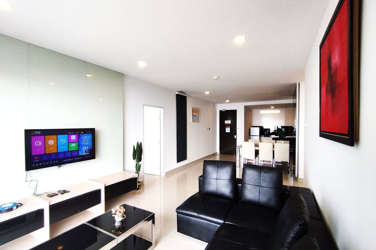 A modern living room with a flat-screen TV, a coffee table, a sofa, and a dining area with chairs.