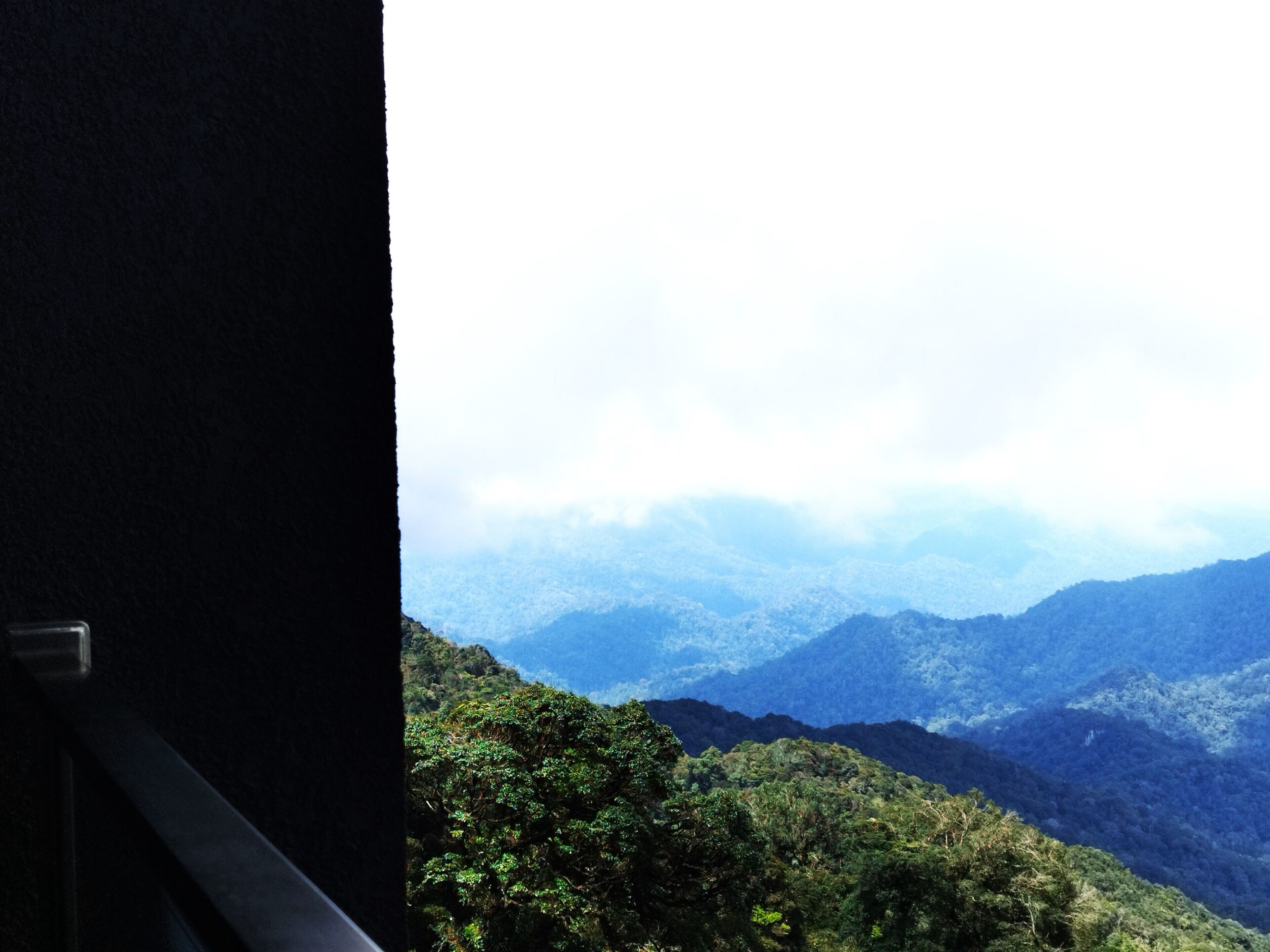 Vista desde una ventana sobre un paisaje montañoso con bosque denso.