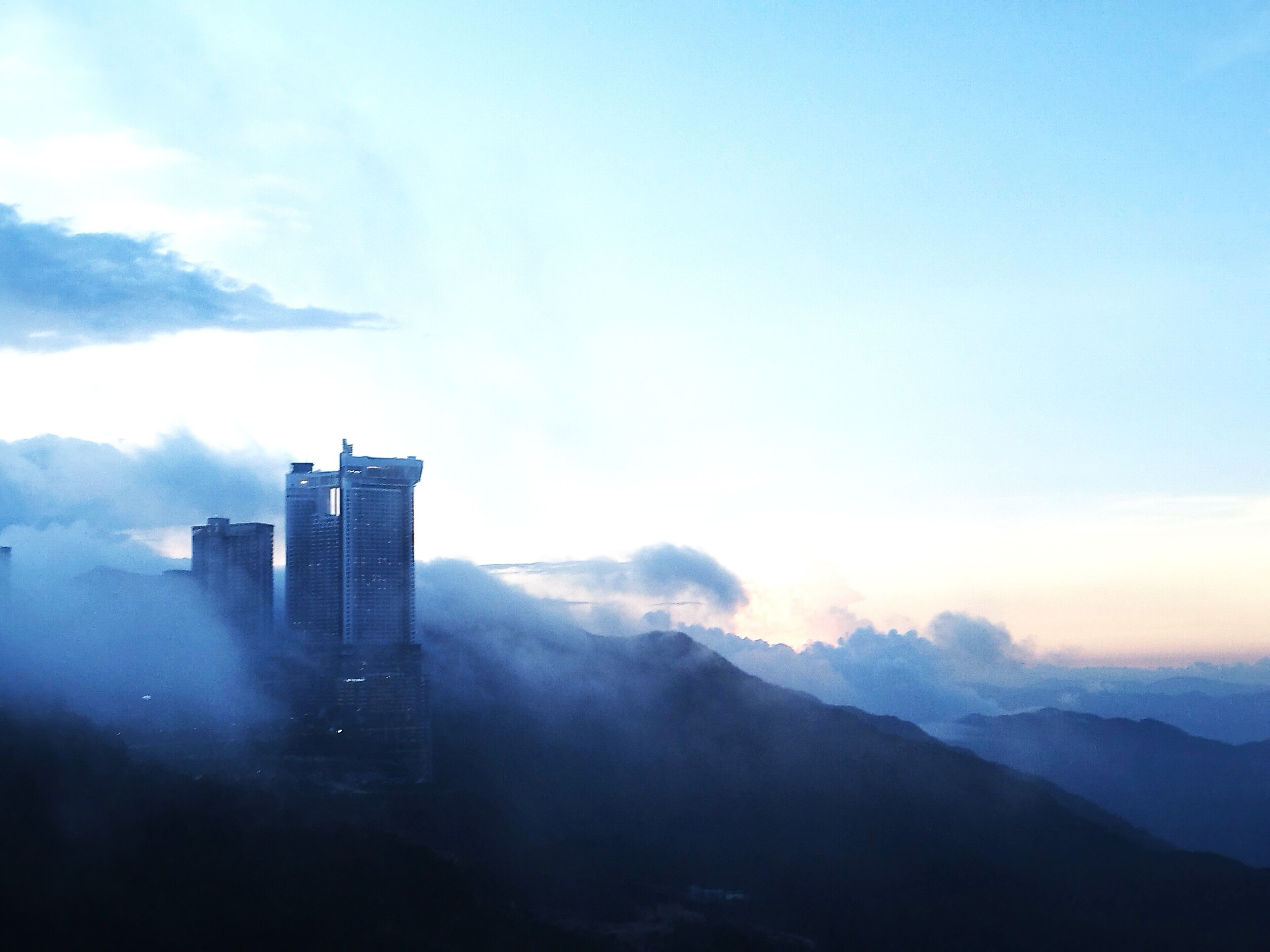 A high-rise building amidst foggy mountains.