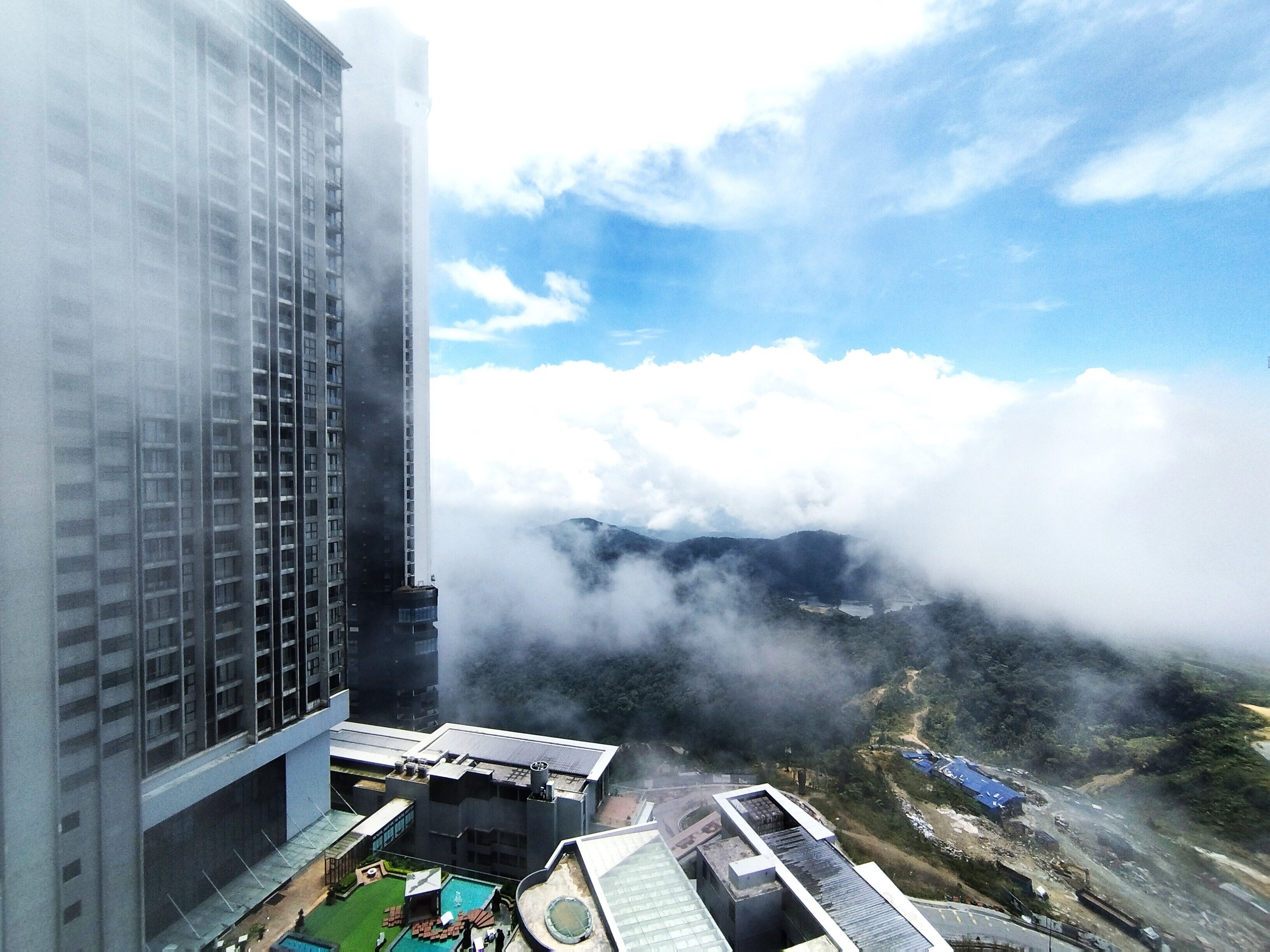 A high-rise building with a rooftop pool and a view of clouds and mountains below.