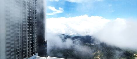 A high-rise building with a rooftop pool and a view of clouds and mountains below.