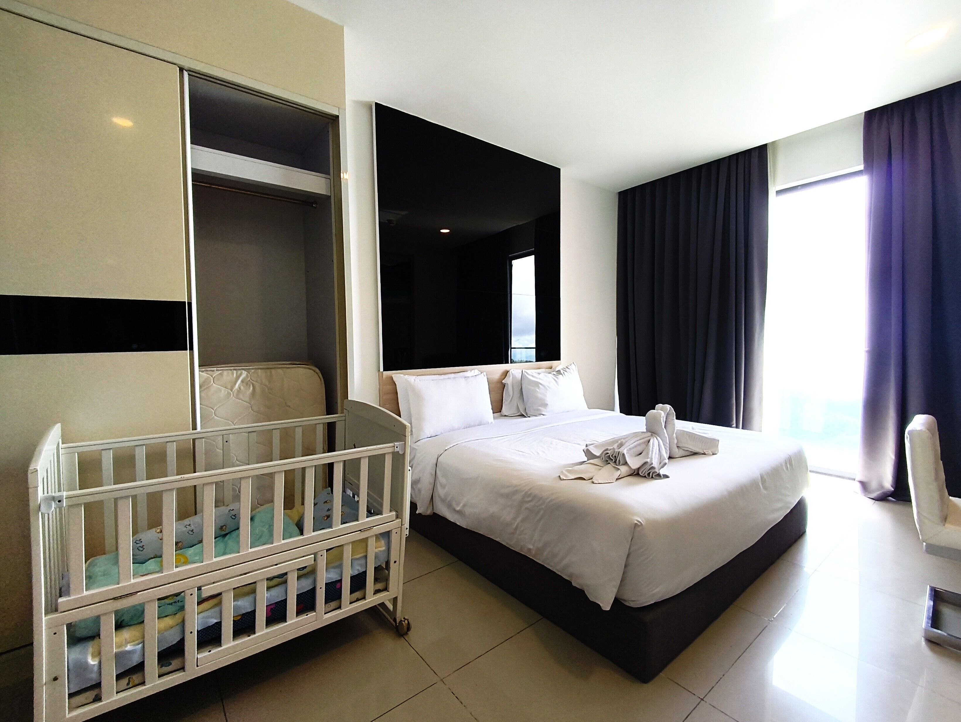 A hotel room with a bed, a crib, a wardrobe, and a view of the outdoors.