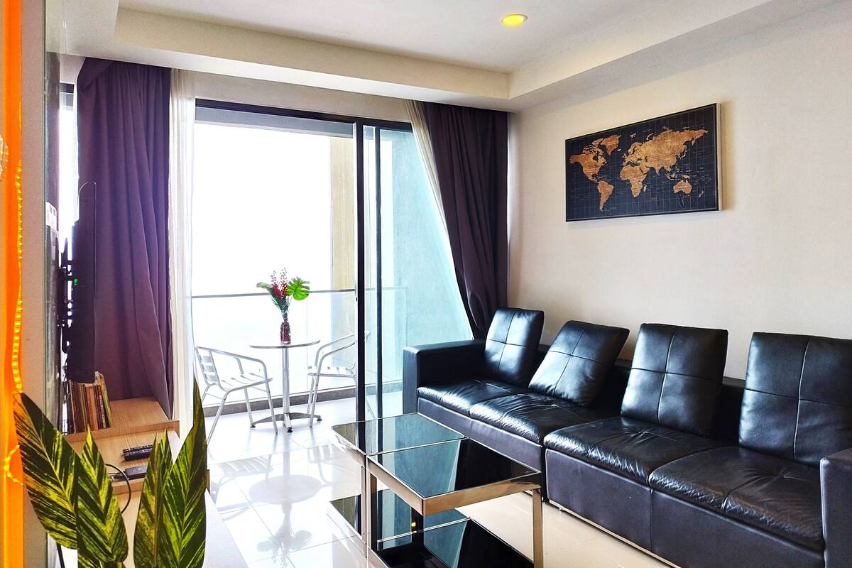 A modern living room with a black leather sofa, a glass coffee table, and a world map on the wall.