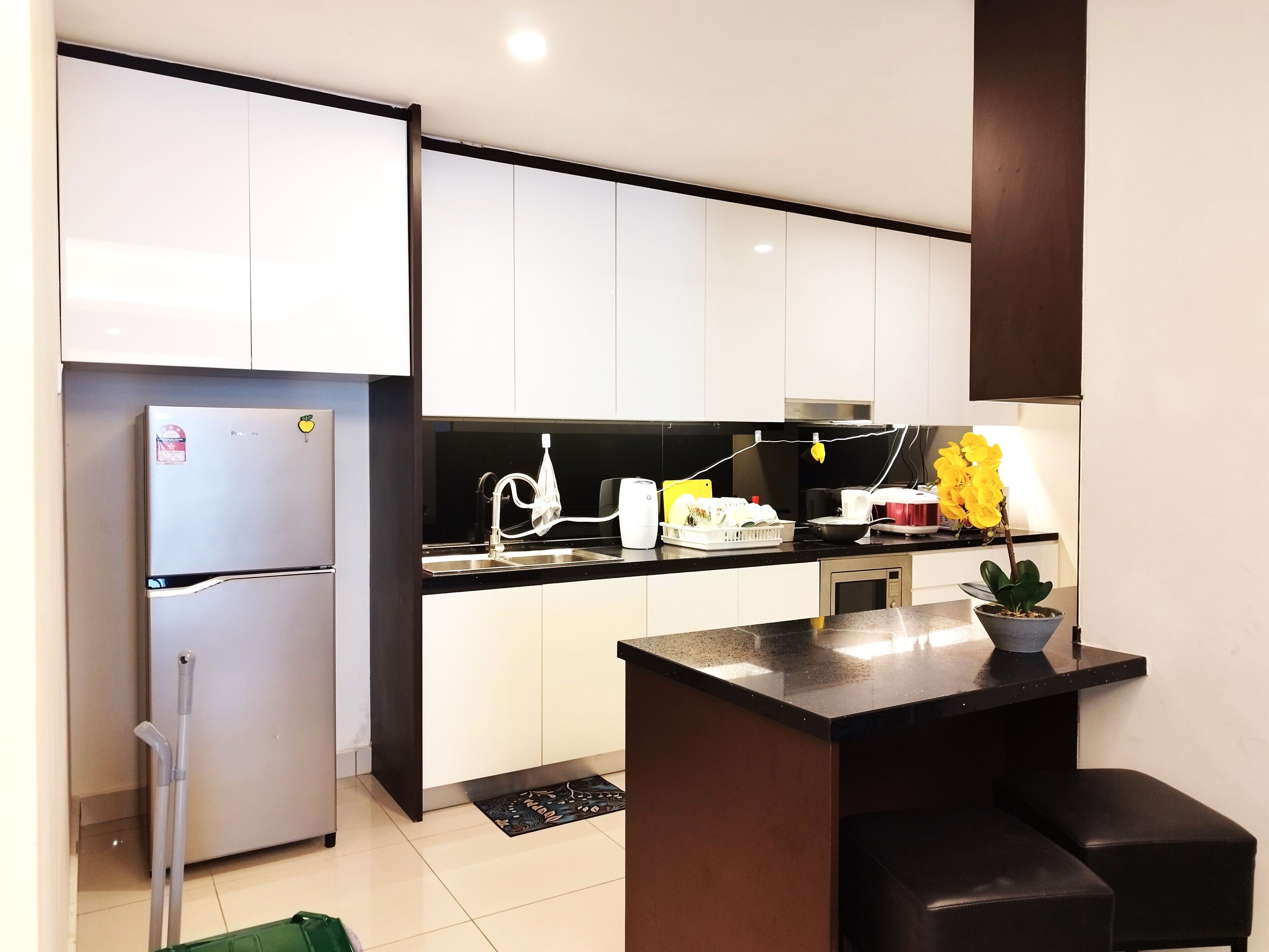 A modern kitchen with white cabinets, a stainless steel refrigerator, a black countertop, and a small potted plant.