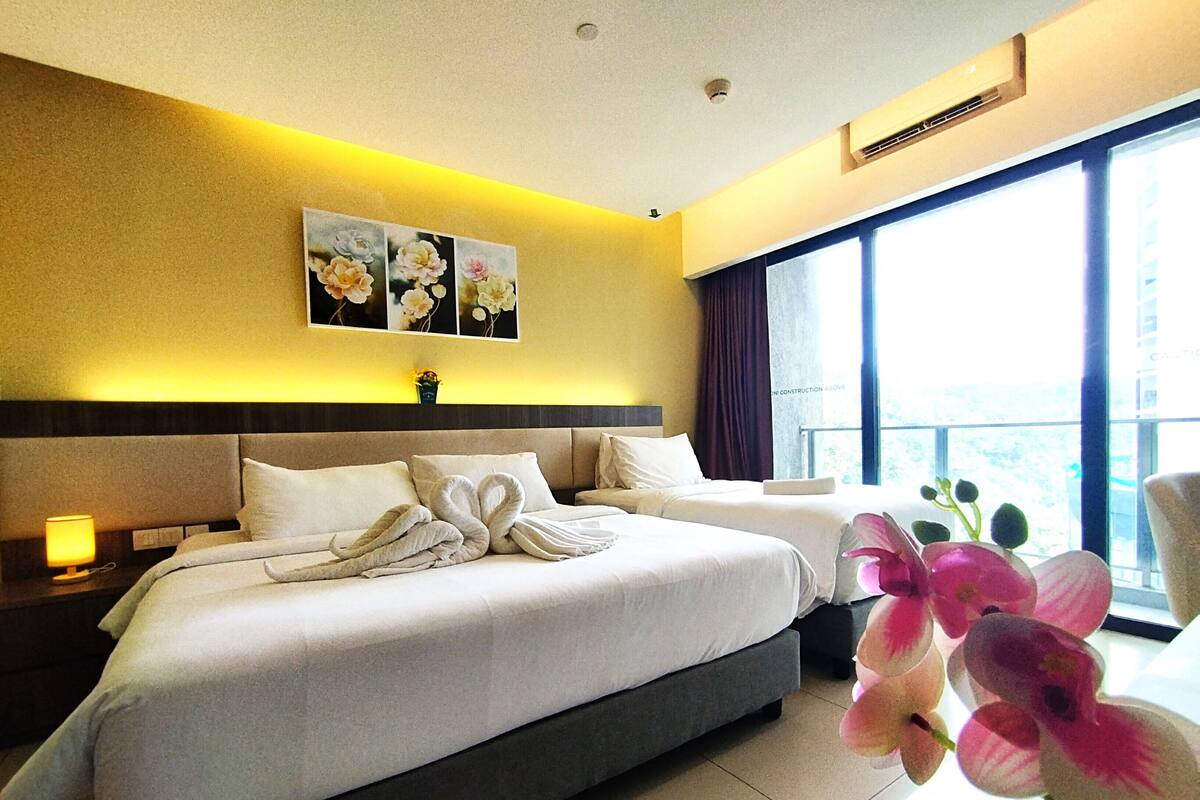 A hotel room with a large bed, two bedside tables, a nightstand, a window with a view, and a wall-mounted air conditioning unit.