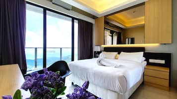 A hotel room with a large bed, a desk, a chair, a view of the mountains, and a balcony.