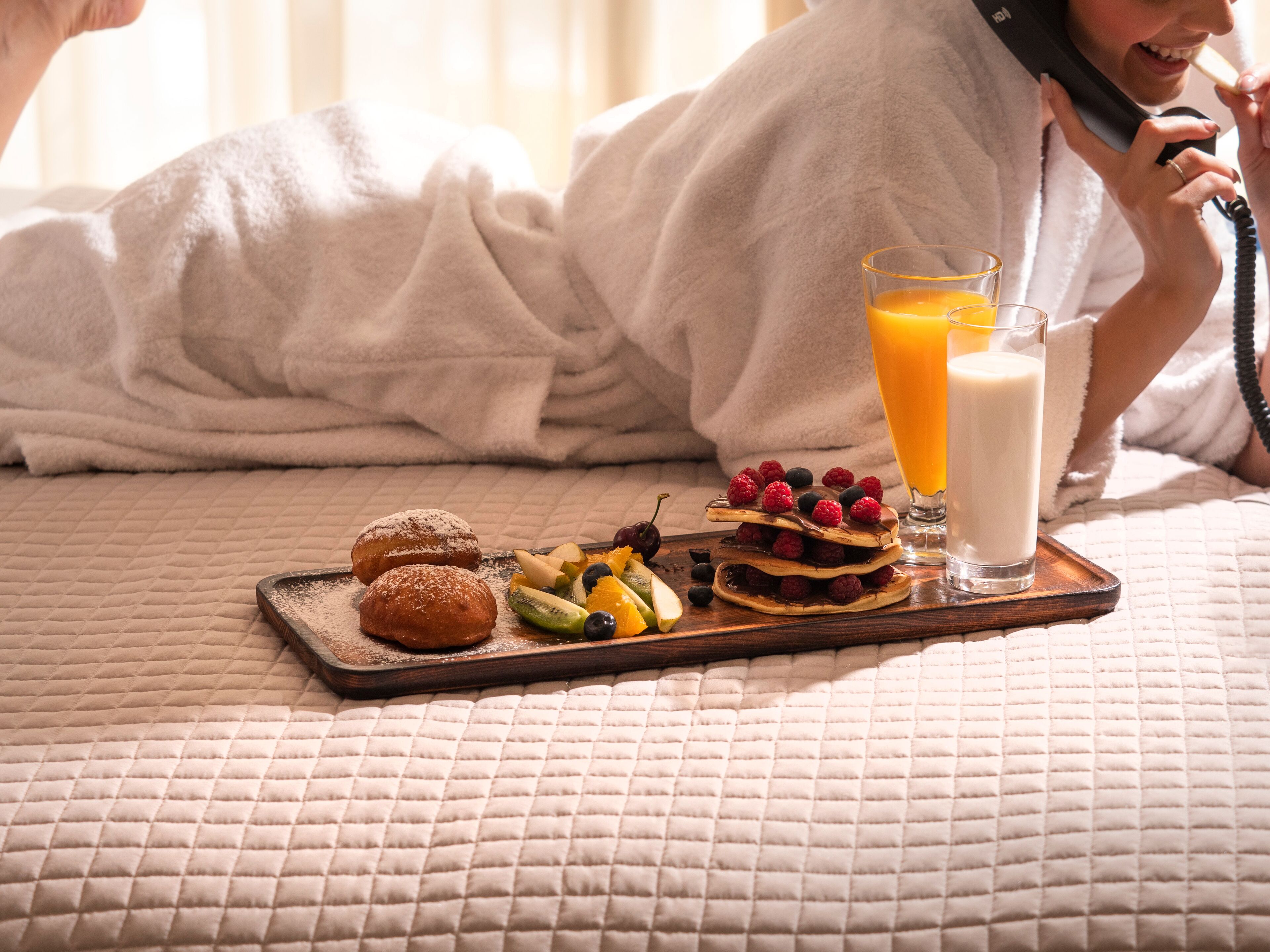 Un lit avec une couverture matelassée, un plateau avec des pâtisseries, des fruits et un verre de jus d’orange.