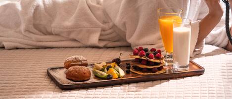 Un lit avec une couverture matelassée, un plateau avec des pâtisseries, des fruits et un verre de jus d’orange.