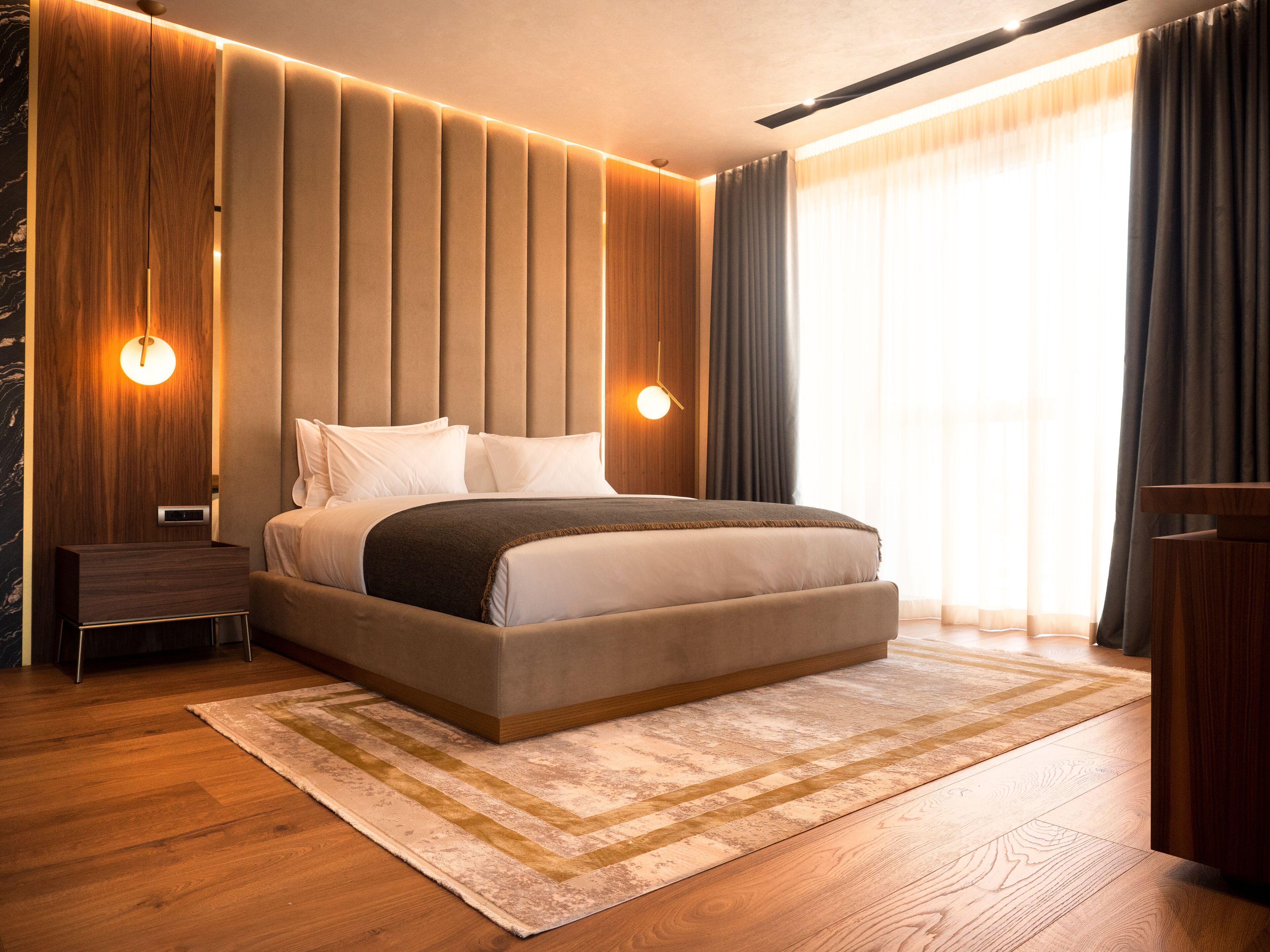 A modern hotel room with a large bed, wooden paneling, and a view of the outdoors.