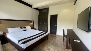 A hotel room with a large bed, a desk, a chair, a wardrobe, and a TV mounted on the wall.