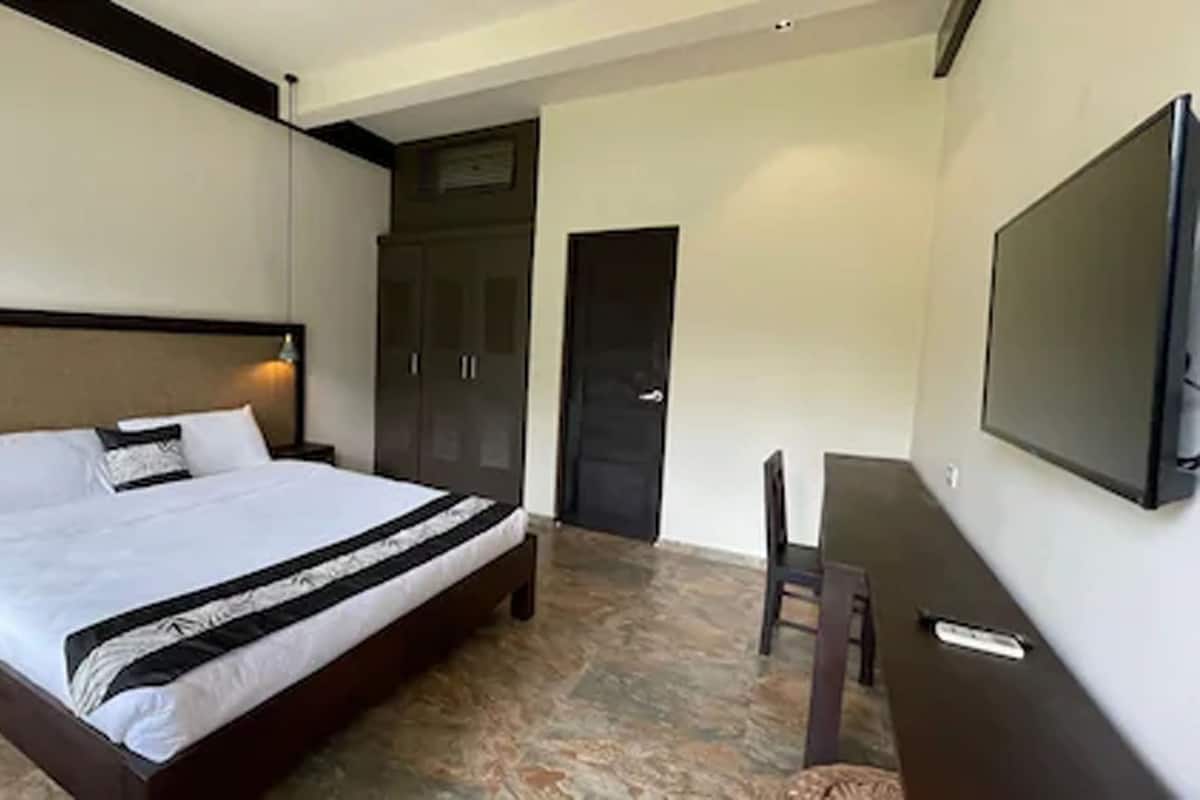 A hotel room with a large bed, a desk, a chair, a wardrobe, and a TV mounted on the wall.