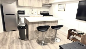A modern kitchen with a refrigerator, microwave, stove, and bar stools.