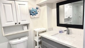 Un baño con inodoro, lavamanos, espejo y repisas con toallas.