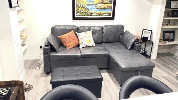 A modern living room with a gray sectional sofa, a small ottoman, and a framed landscape painting on the wall.