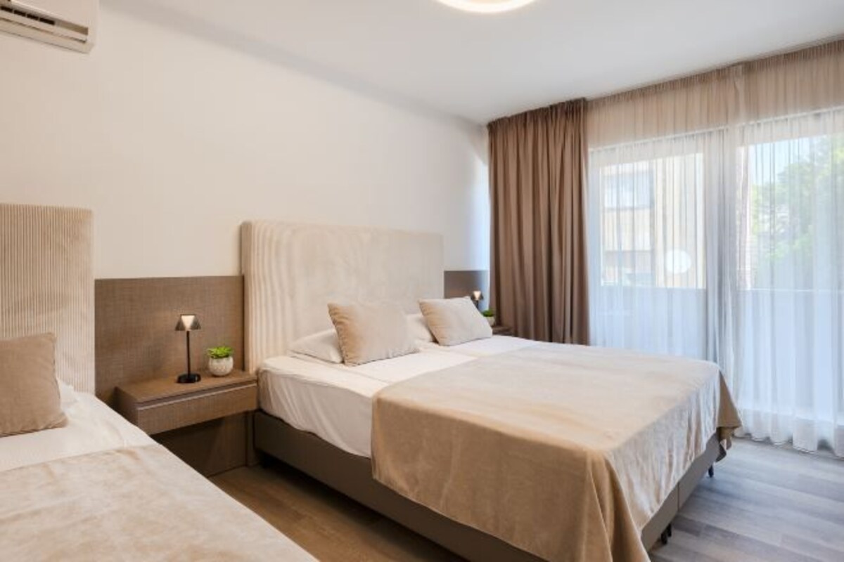 A hotel room with a large bed, bedside tables, a lamp, and curtains.