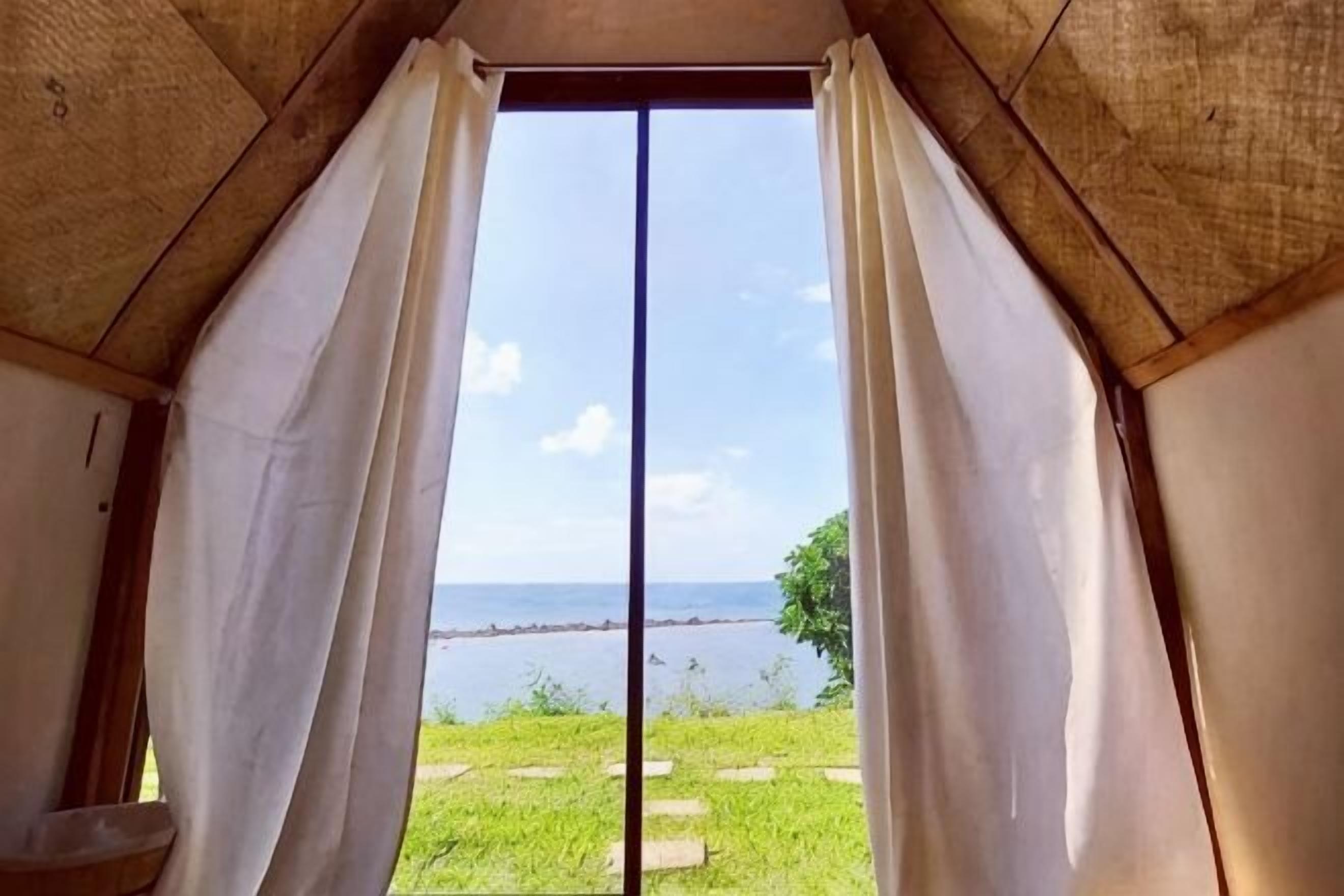 A room with a view of a body of water through a large window with curtains.