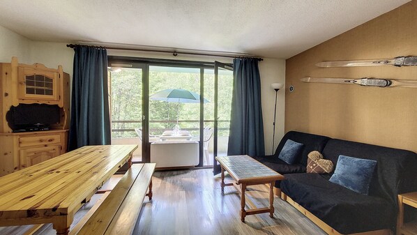 Une pièce avec une table en bois, un canapé, un téléviseur et une porte-fenêtre coulissante donnant sur un balcon.