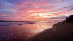 Une plage avec un ciel au coucher du soleil, des vagues calmes et des empreintes de pas dans le sable.