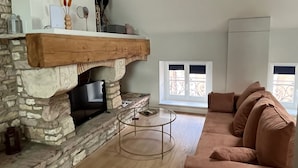 Una sala acogedora con chimenea de piedra, repisa de madera, un sofá confortable y una mesita redonda.