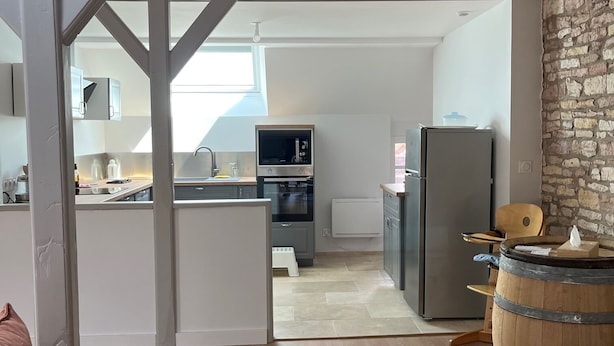 Una cocina moderna con una isla central, un comedor con un barril de madera y una zona de estar acogedora con un sofá rosa.