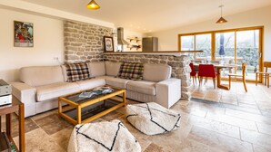 A cozy living room with a stone wall, a sofa, a coffee table, and a dining area with a view.