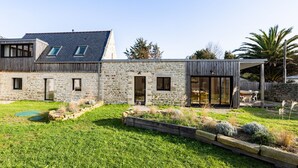 A modern house with stone walls, a wooden deck, and a grassy yard.