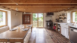 A modern kitchen with a large island, a stove, and a sink. There is a stone wall and a view of greenery outside. - Gîtes de Lézinadou - 6 personnes - Plomeur La Torche (plomeur)