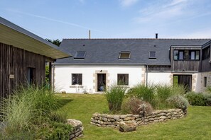 A modern house with a sloped roof, a stone wall, and a small garden with grass and plants. - Gîtes de Lézinadou - 6 personnes - Plomeur La Torche (plomeur)
