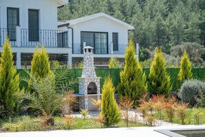 A modern two-story building with a stone fireplace, surrounded by a variety of greenery and a well-maintained garden. - Green Hills Family-Friendly Luxury Villa - Fethiye (Fethiye)