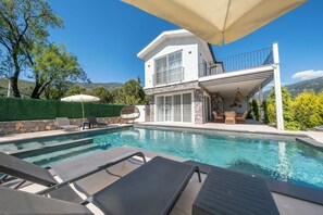 A pool area with lounge chairs, a covered seating area, and a stone wall.