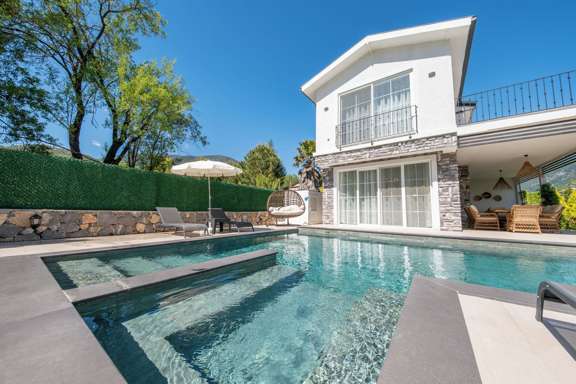 Une maison moderne à deux étages, dotée d’une piscine, de murs en pierre et d’un espace salon extérieur.