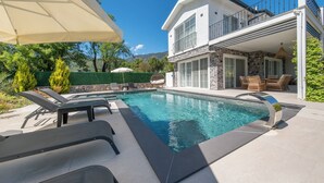 Une maison moderne dotée d’une piscine, de mobilier d’extérieur et d’une façade en pierre.
