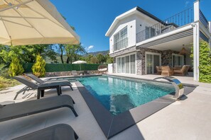 Ein modernes Haus mit Swimmingpool, Gartenmöbeln und einer Fassade aus Naturstein.